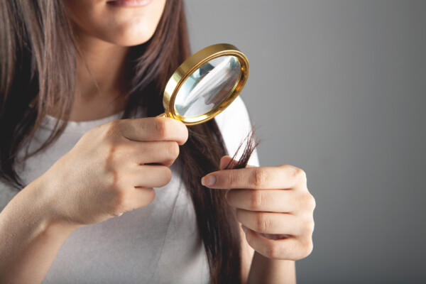 young woman looking at her hair with a magnifying glass